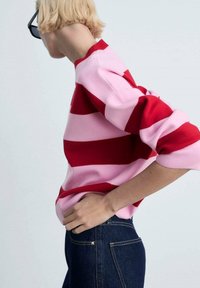 Pull en tricot rayé rouge et rose ; doté d'un col rond et de poignets côtelés ; associé à un jean en denim foncé.