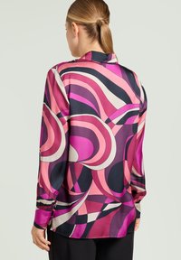 Silkebluse med et farverigt abstrakt mønster i pink, lilla og marineblå; lange ærmer og klassisk krave med sideslids ved kanten.