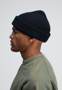 Zwarte gebreide beanie met geribbelde textuur, taps toelopende bovenkant en omgeslagen boord. Gemaakt in combinatie met een lichtgroene crewneck sweatshirt.