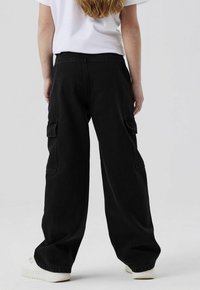 Crne široke cargo hlače s visokim strukom, bočnim džepovima i opuštenim krojem. Izrađene su od teksturirane denim tkanine i imaju minimalistički dizajn.