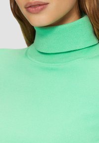 Lichtgroene coltrui met een strak ontwerp, gladde textuur en geribbelde kraag. Heeft een naadloze uitstraling zonder zichtbare bevestigingsmiddelen.