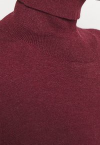 Suéter burdeos de cuello vuelto, material de punto suave, diseño ajustado, cuello y dobladillo acanalados, ligera textura visible en la superficie del tejido.