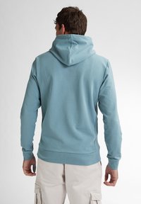 Sudadera azul clara con una capucha amplia, mangas largas y puños acanalados. Fabricada con un tejido suave, presenta un diseño simple sin patrones.