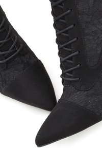 Botines negros con diseño de punta afilada, paneles de tela y detalles de encaje. Material de ante con detalles texturizados y cordones negros.