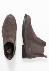 Brown suede ankle boots with elastic side panels, rounded toes, and small black rubber heels. Detailed stitching enhances the design.