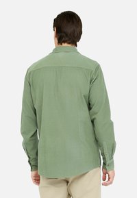 Camisa de manga larga verde en un tejido texturizado con corte recto, puños con botón y un yugo en contraste en la parte posterior.