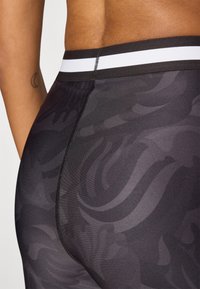 Black patterned leggings feature a wide elastic waistband with a white stripe, smooth texture, and subtle abstract designs.