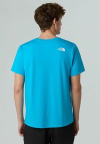 T-shirt a maniche corte in tessuto blu brillante. Presenta un collo a giro e un dettaglio del logo bianco sulla parte superiore della schiena. Texture liscia.