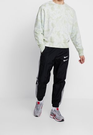 Lichtgroene tie-dye sweatshirt met lange mouwen, gecombineerd met zwarte nylon joggingbroek met een wit Nike-logo en grijze zijaccenten.