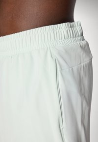 Helle mintgrüne Sportshorts mit elastischem Bund, Seitentasche und glatter Textur, die eine lockere, bequeme Passform bieten.