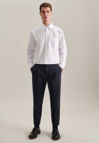Witte overhemd met lange mouwen, knoopsluiting aan de voorkant en een zak; gecombineerd met donkerblauwe broek en zwarte schoenen. Eenvoudig ontwerp, gladde textuur.