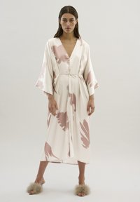 Robe en soie couleur crème avec un motif abstrait rose, dotée d'un décolleté en V profond, de manches larges et d'une taille nouée. Texture lisse.