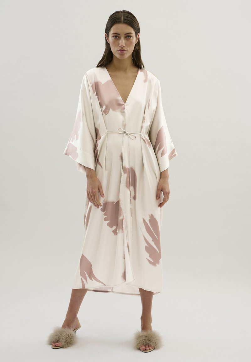 Robe en soie couleur crème avec un motif abstrait rose, dotée d'un décolleté en V profond, de manches larges et d'une taille nouée. Texture lisse.