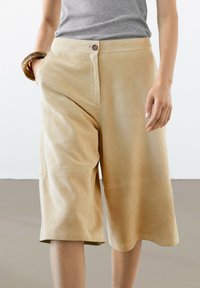 Beige faux suede culottes met zijzakken, voorzien van een knoopsluiting en een ontspannen pasvorm die net onder de knie valt.
