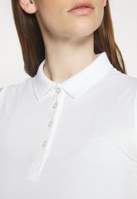 Biała koszulka polo z strukturalnej bawełny, klasycznym kołnierzykiem i sześcioma guzikami; posiada małe haftowane logo "CK".