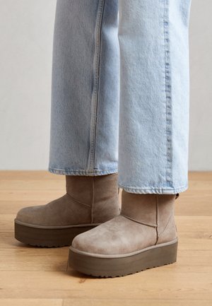 Jean bleu clair associé à des bottines beige en daim à plateforme sur un sol en bois.