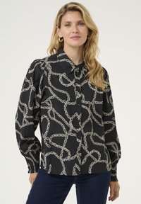 Camicia nera con bottoni, caratterizzata da un design a catena bianca, con colletto e maniche a sbuffo. Tessuto liscio e polsini aderenti.