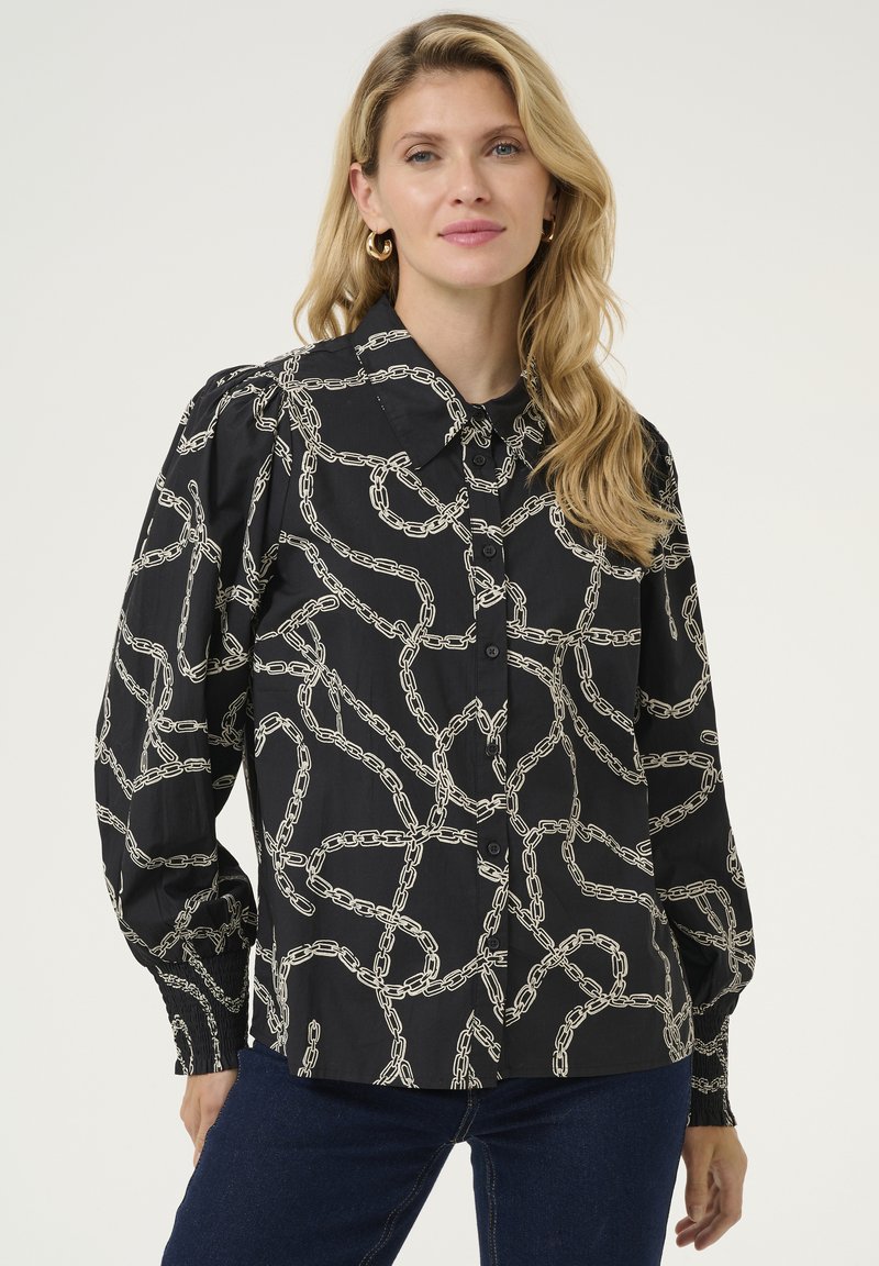 Camicia nera con bottoni, caratterizzata da un design a catena bianca, con colletto e maniche a sbuffo. Tessuto liscio e polsini aderenti.