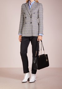 Veste croisée à carreaux gris portée sur une chemise bleu rayé, associée à un pantalon noir et des bottines blanches à fermeture éclair, tenant un sac à main noir.