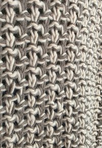 Dziergany materiał w kolorze szarym i kremowym, z fakturowanym, otwartym wzorem o splocie z przeplatanych ściegów i miękkim, puszystym wyglądzie.
