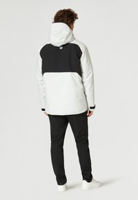 Vit och svart jacka med huva, med en svart övre del och vit nedre del. Designen är elegant med en något glänsande yta.