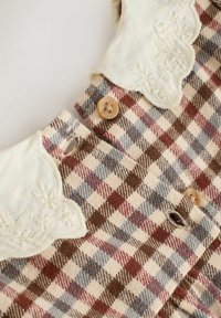 Robe à carreaux avec un col crème à bords festonnés. Présente un motif à carreaux marron, rouge et bleu. Comprend des boutons en bois et des détails floraux brodés.