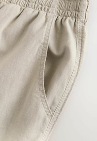Lys beige linned shorts med en rynket talje, sidelomme og synlige syninger. Stoffet fremstår tekstureret og åndbart.