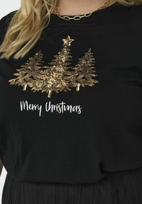 Svart t-shirt med gyllene paljetter i form av julgranar och texten "God Jul" i vitt under designen. Enkla, festliga grafiker.