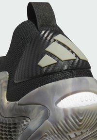 Scarpa sportiva nera con upper testurizzato, caratterizzata da un logo prominente e suola trasparente. Il tallone ha un linguetta per una facile calzata.