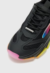 Black athletic shoe featuring mesh panels, laces, and a colorful gradient sole transitioning from yellow to pink. Silver branding detail present.