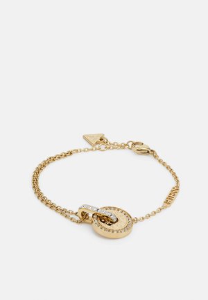 Pulseira de ouro com um pendente redondo que apresenta pedras transparentes e detalhes gravados. As correntes estão ligadas, com um fecho para fechar.