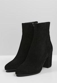 Bottines en suede noir avec un talon épais, un bout pointu et un zip sur le côté. Texture lisse et design épuré.