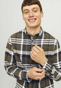 Bruin en marineblauw geblokt shirt met witte accenten, met knoopsluiting bij de kraag en lange mouwen. Model past de manchet aan en toont knoopdetails en stoftextuur.
