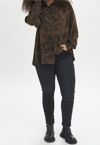 Brown button-up shirt with black abstract pattern, paired with dark jeans featuring ankle zippers and black combat boots. Soft texture.