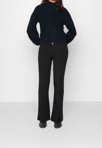 Black flared pants with front slits paired with a dark, textured, ribbed cropped sweater featuring voluminous sleeves.