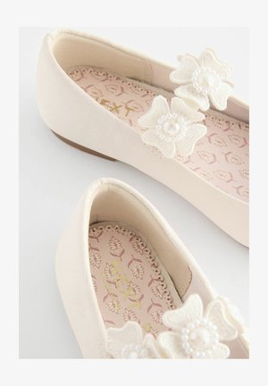 Balerini bej deschis, confecționați dintr-un material moale, cu flori brodate și accente de perle. Branțul prezintă un model floral pe un fundal roz.