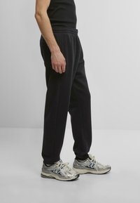 Black jersey sweatpants with an elastic waistband, featuring a relaxed fit. Paired with silver running shoes with blue accents.