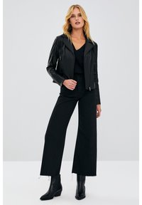 Black faux leather motorcycle jacket with a cropped design, accompanied by a black top and wide-leg black pants. Glossy finish, zip details.
