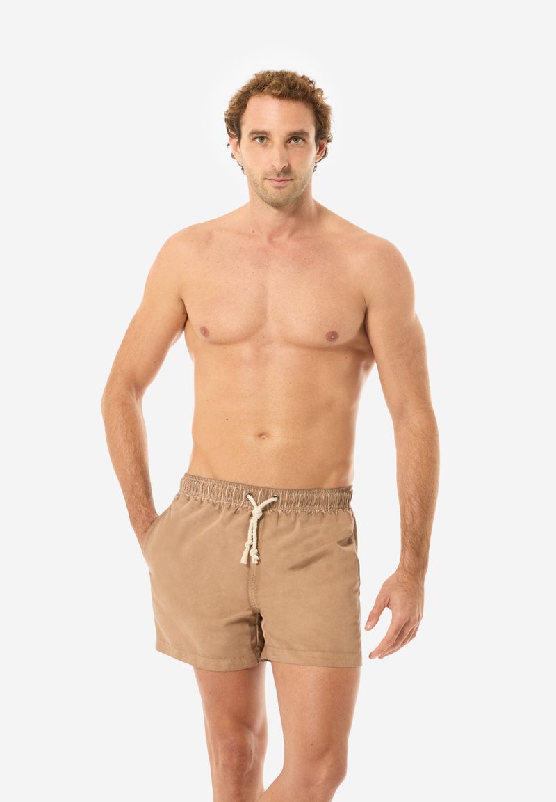 Pantaloni da bagno color tan realizzati in tessuto morbido, dotati di un cinturino elastico con coulisse e tasche laterali. Texture liscia, design semplice.