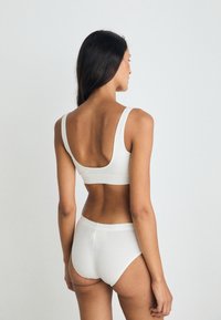Bralette blanc sans couture avec de larges bretelles et un dos plongeant, associé à des culottes taille haute assorties. Tissu doux et extensible, design minimal.