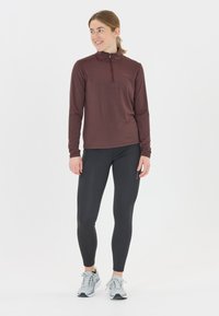 Bordeaux langærmet top med halvlåsekrave, parret med sorte leggings og grå sportsko. Glat stof; atletisk pasform.