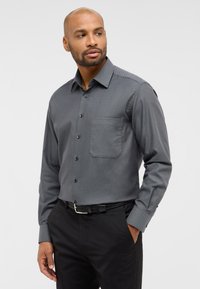 Grau gemustertes Langarmhemd mit Button-Down-Kragen, einer einzelnen Brusttasche und schwarzen Knöpfen, kombiniert mit schwarzen Hosen.