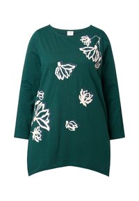 Grünes Baumwolloberteil mit 3/4-Ärmeln, das mit weißen und violetten Blumenmustern verziert ist. Gerundeter Saum mit leicht längerem Rückenteil. Glatte Textur.