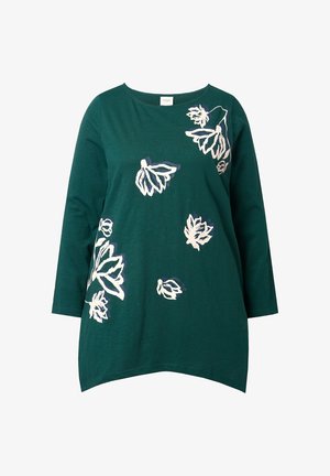 Grøn bomuldsbluse med 3/4 ærmer, prydet med hvide og lilla blomsterdesigns. Rundet kant med lidt længere ryg. Glat tekstur.