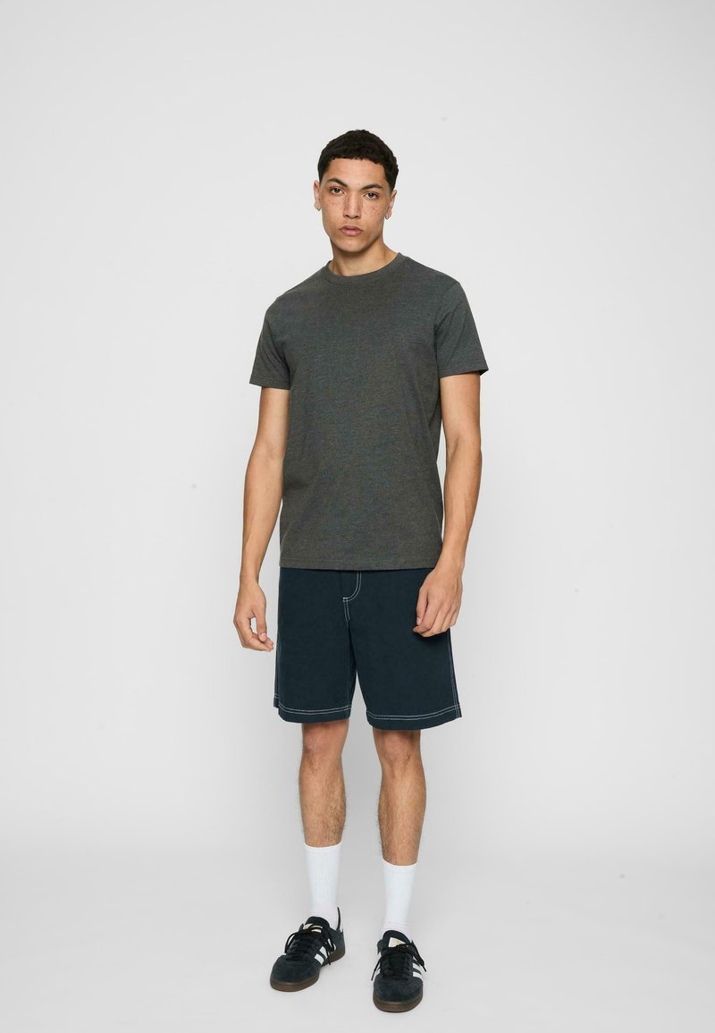 Un tricou din bumbac gri închis asociat cu pantaloni scurți din denim închis, având cusături albe, șosete albe până la gleznă și adidași negri.