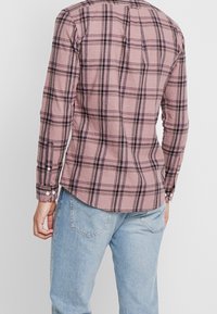 Koszula w kratę z długim rękawem w stonowanym różowym kolorze z czarnymi kratkami, z zaokrąglonym dołem i zapinanymi mankietami. Miękka w dotyku, o casualowym kroju.