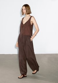 Brun linne jumpsuit med en figursydd, ärmlös topp, sänkt midja och vida byxor. Har sidofickor och en avslappnad silhuett.