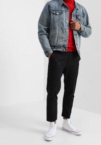 Hellblaues Jeansjacke, rotes Hemd, schwarze Hose und weiße High-Top-Sneaker. Die Jacke hat zwei vordere Taschen und einen Knopfverschluss.