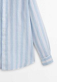 Chemise à manches longues rayée verticalement bleu clair et blanc avec des boutons, montrée du torse au poignet sur un fond blanc uni.