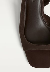 Bruna mockasinsandaler med en slät lädersula. Designen har ett brett rem och en rund tå. Sulan är texturerad och platt.
